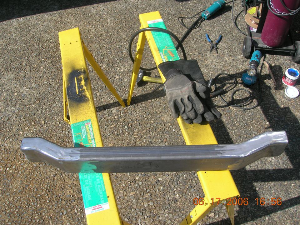 Fabricated metal bar on yellow sawhorses with welding tools and gloves nearby