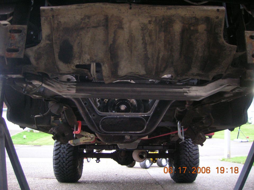 Undercarriage of a lifted Ford Bronco on jack stands showing crossmember, diff, and off-road tires