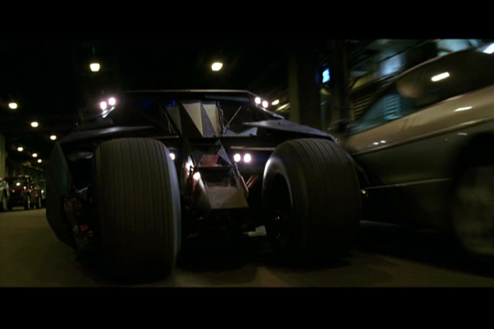 Movie still of black armored Batmobile at night from low rear angle passing a car