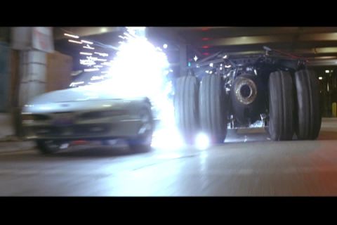 1994 Ford Probe - A car is seen with sparks erupting as it drives alongside a large, multi-wheeled vehicle.