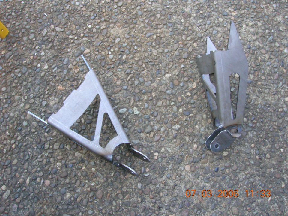 Two welded bare steel fabricated brackets on gravel ground