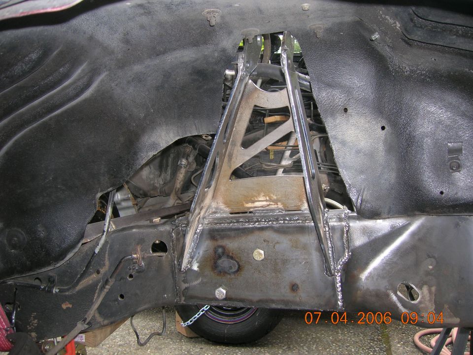 Fabricated steel bracket welded to a frame crossmember beneath a black undercoated floor pan