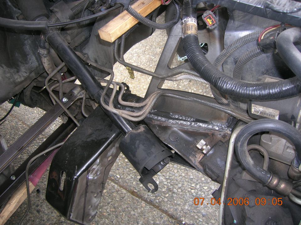 Truck front-end fabrication showing freshly welded crossmember bracket and wiring harnesses