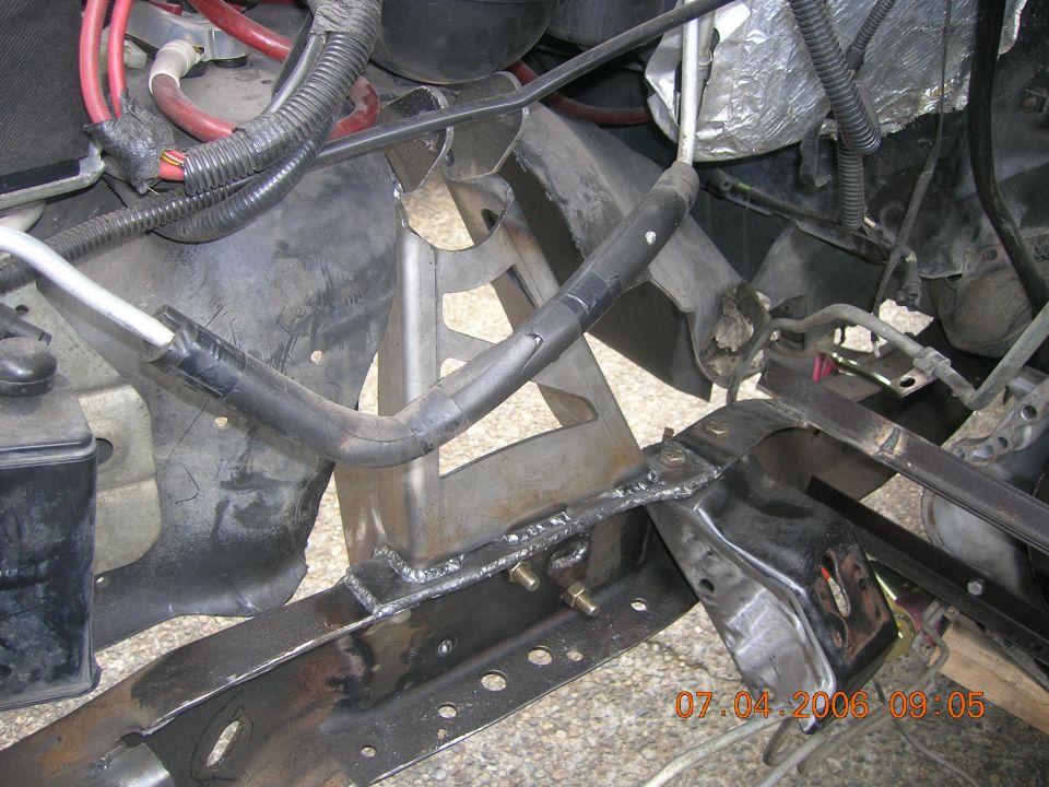 Welded metal bracket on black frame with hoses and wiring, vehicle under repair
