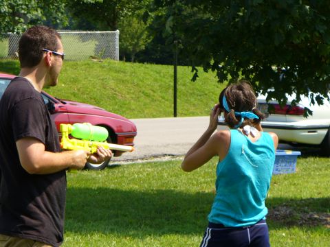 1991 Ford Probe - Two people with water guns stand near cars in a grassy area on a sunny day.
