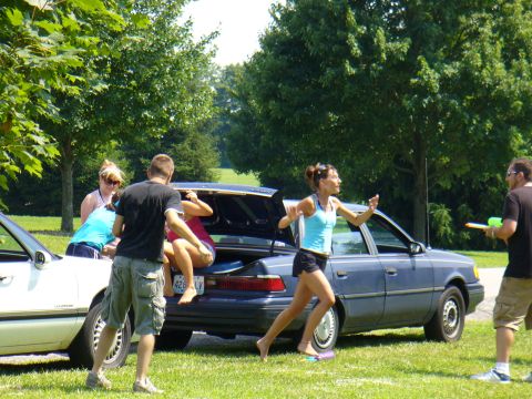1991 Ford Probe - People gathered around a blue sedan with its trunk open, suggesting a casual outdoor activity.