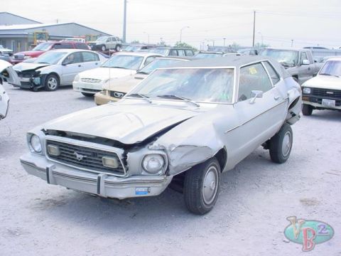 1978 Ford Mustang II - Damaged 1978 Ford Mustang II coupe sits in a salvage yard with other wrecked cars.