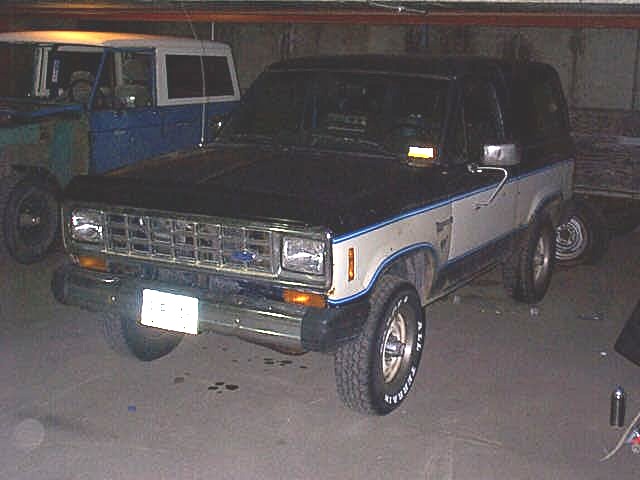 Black-and-silver Ford Bronco II SUV parked in a dim garage, front 3/4 view.