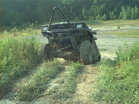 1986 Ford Bronco - This heavily modified off-road vehicle navigates a muddy track through overgrown vegetation.