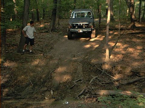 1986 Ford Bronco - A man stands near a dark Ford Bronco navigating a muddy, wooded trail.