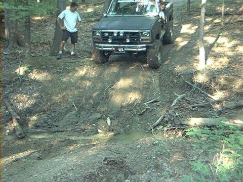 1986 Ford Bronco - A dark pickup truck navigates a steep, muddy hill with a person watching nearby.