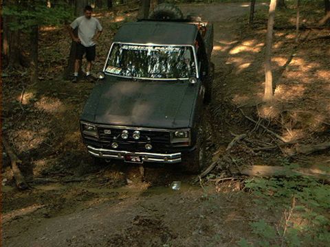 1986 Ford Bronco - Ford F-150 pickup truck navigating a muddy trail in a wooded area.