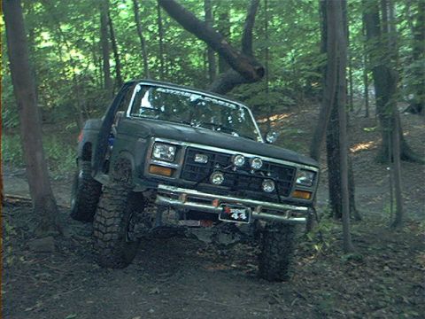1986 Ford Bronco - This SUV is navigating a muddy trail surrounded by trees.