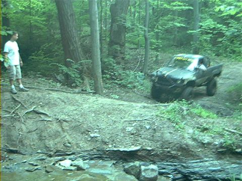 1986 Ford Bronco - An off-road vehicle navigates a muddy trail through a wooded area.