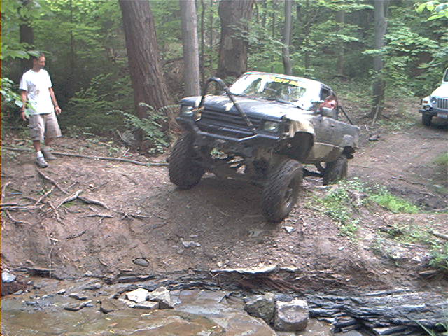 Modified off-road truck climbing a dirt incline, another Jeep visible in background