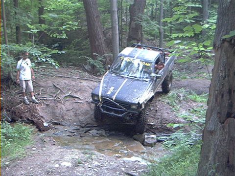 1986 Ford Bronco - Off-road Toyota pickup truck navigating a challenging muddy trail with a person watching.