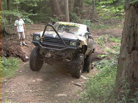 1986 Ford Bronco - This modified truck is tackling a challenging off-road course in a wooded area.