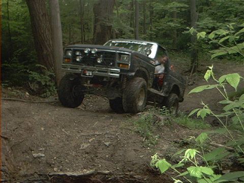 1986 Ford Bronco - This modified SUV navigates a steep, muddy incline in a wooded area.