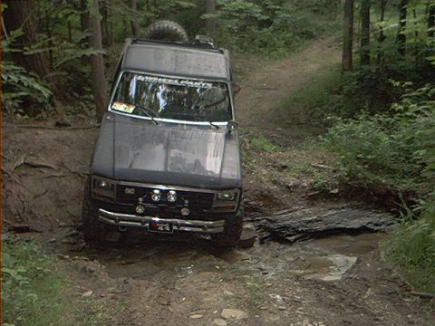 1986 Ford Bronco - Ford Bronco tackling an off-road trail with muddy water and rocks.