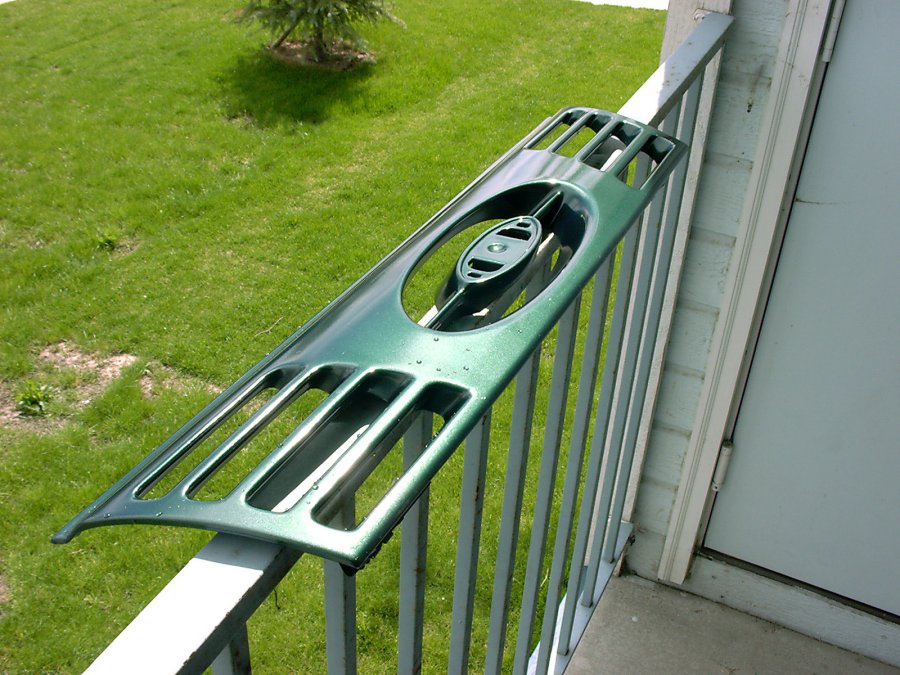 Metallic green Ford grille panel with oval emblem cutout balanced on a balcony railing over a lawn