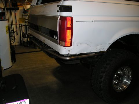 1993 Ford Bronco - The rear section of a white SUV shows a custom bumper and significant body damage near the wheel well.