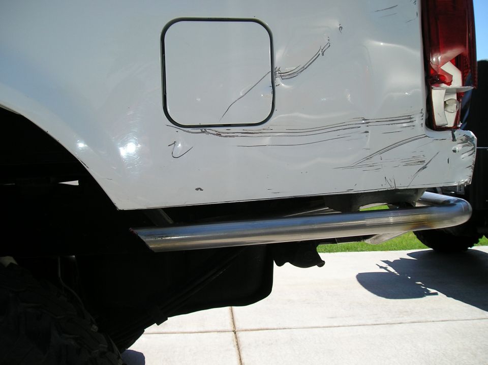 Damaged white Bronco rear quarter panel with scrapes near fuel door and chrome nerf bar