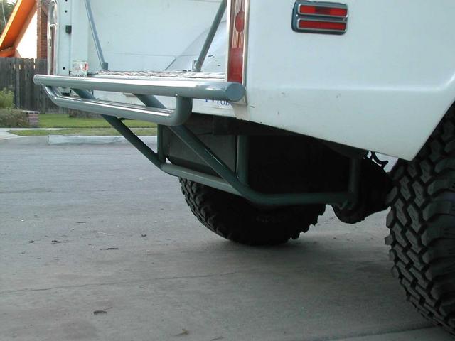 Tubular rear bumper and step under a white truck with mud tires