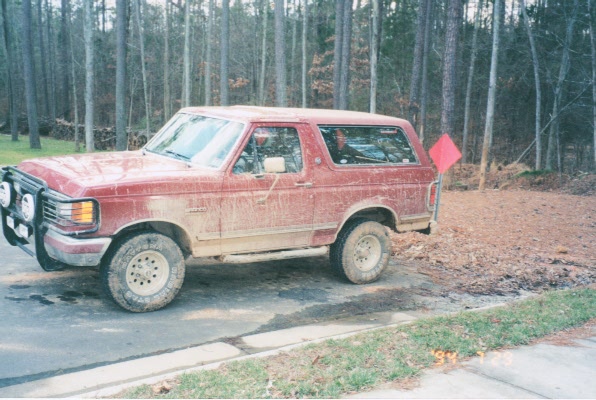 Mud-splattered red two-door Ford Bronco SUV parked on driveway, front 3/4 view