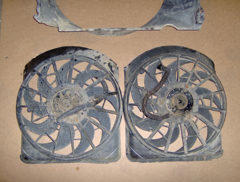 1978 Ford Bronco - Two used black plastic electric cooling fan assemblies laid side by side on a cardboard-covered floor, each with a multi-blade fan in a squ…