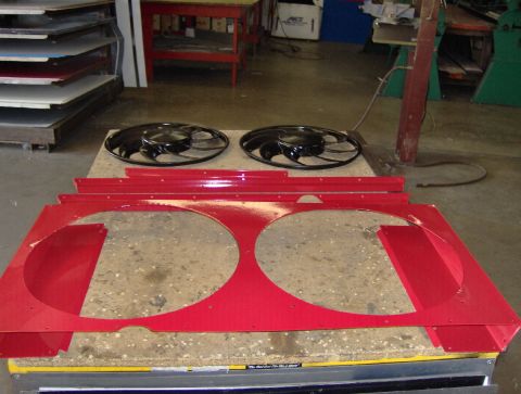 1978 Ford Bronco - A freshly powder-coated red fan shroud laid out on a shop bench, with two large circular fan cutouts, riveted side flanges and matching red…