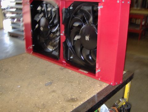 1978 Ford Bronco - A fabricated red-painted radiator shroud standing on a workbench, housing two black electric cooling fans of different diameters bolted thr…