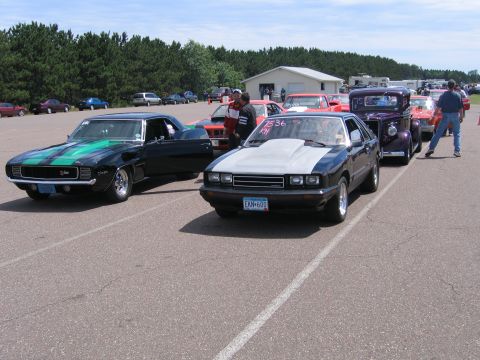 1989 Ford Mustang - A line of cars at what appears to be a drag strip or car show, with a Ford Capri in the foreground.