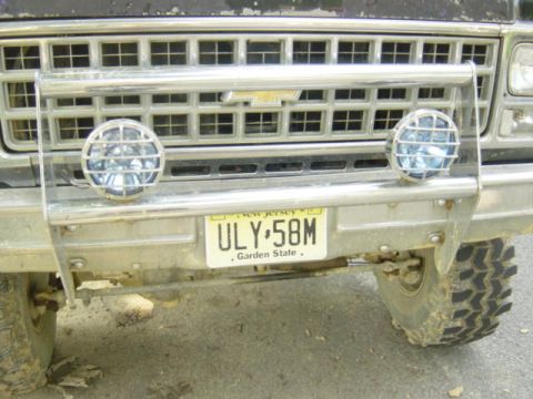 1987 Suzuki Samurai - Close-up of a truck's front grille and bumper, a brush guard and auxiliary lights.