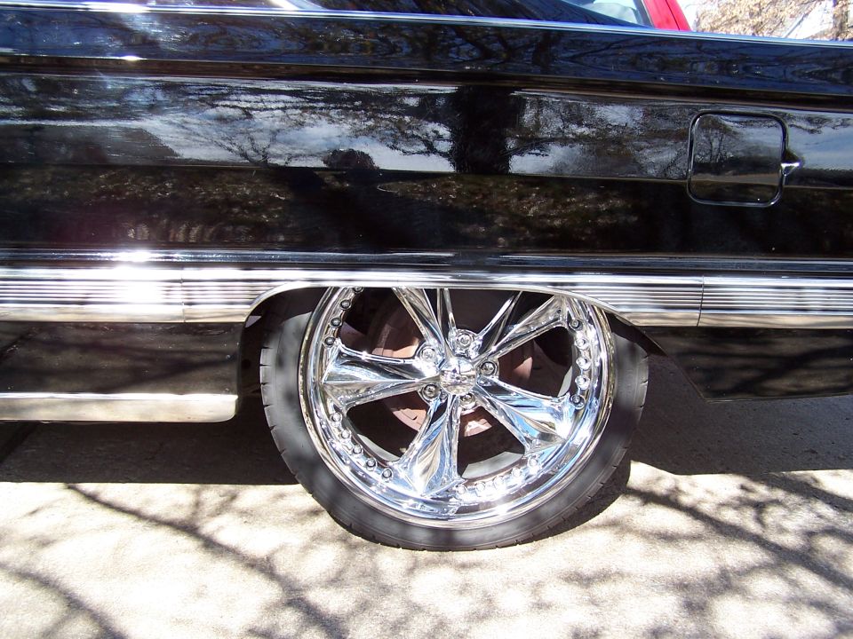 Chrome twisted-spoke wheel tucked under the rear quarter of a black classic car