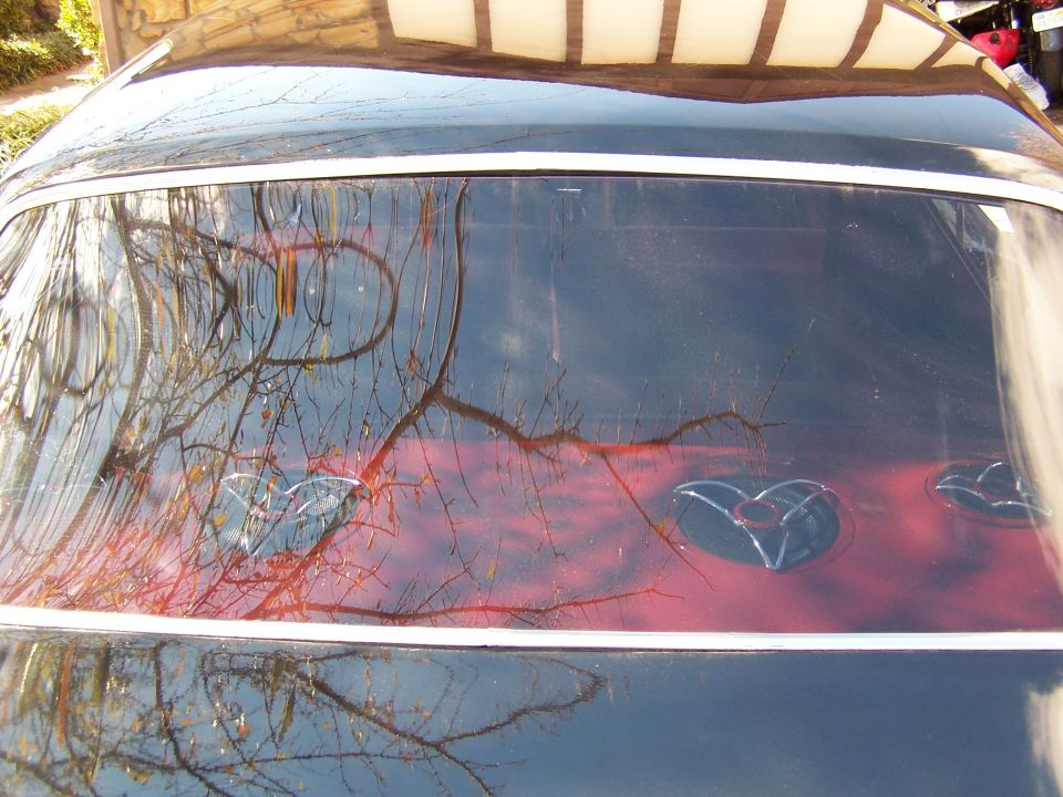 Rear window of a dark blue hardtop showing three chrome speaker grilles on a red package tray