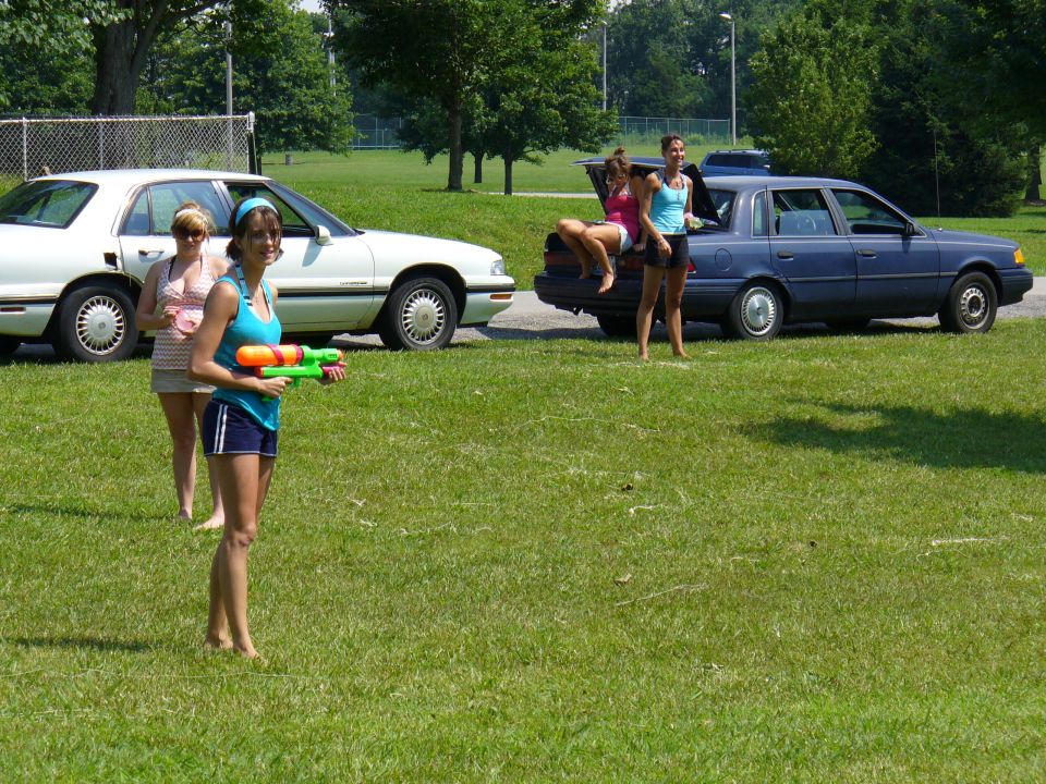Two sedans parked on a lawn with three women standing around one of them