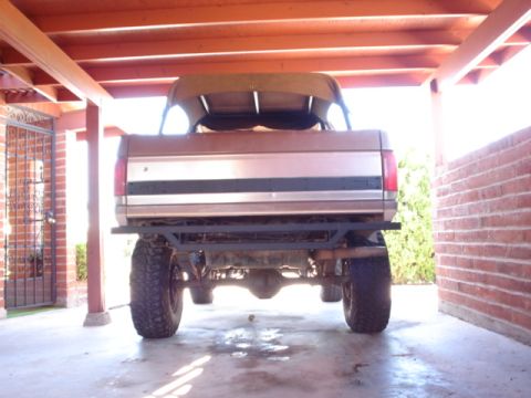 1989 Ford Bronco - Rear view of a lifted 1987 Ford Bronco with a soft top, parked under a carport.