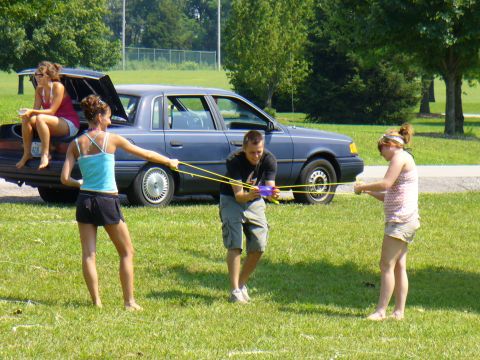 1991 Ford Probe - Teens play with a water gun next to a blue sedan on a sunny day.
