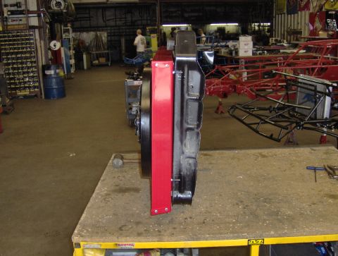 1978 Ford Bronco - Edge-on view of a black radiator with a fabricated red sheet-metal fan shroud riveted to its face, standing upright on a fab-shop workbench…