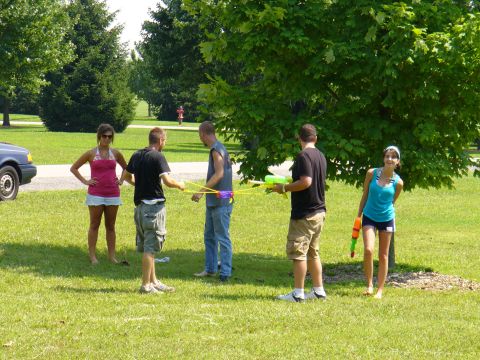 1991 Ford Probe - A blue car is parked on the side of a path in a park where a group of people are gathered.