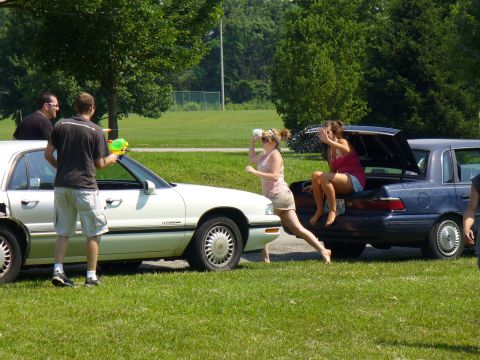 1991 Ford Probe - People engaged in a water gun fight near two parked cars on a sunny day.