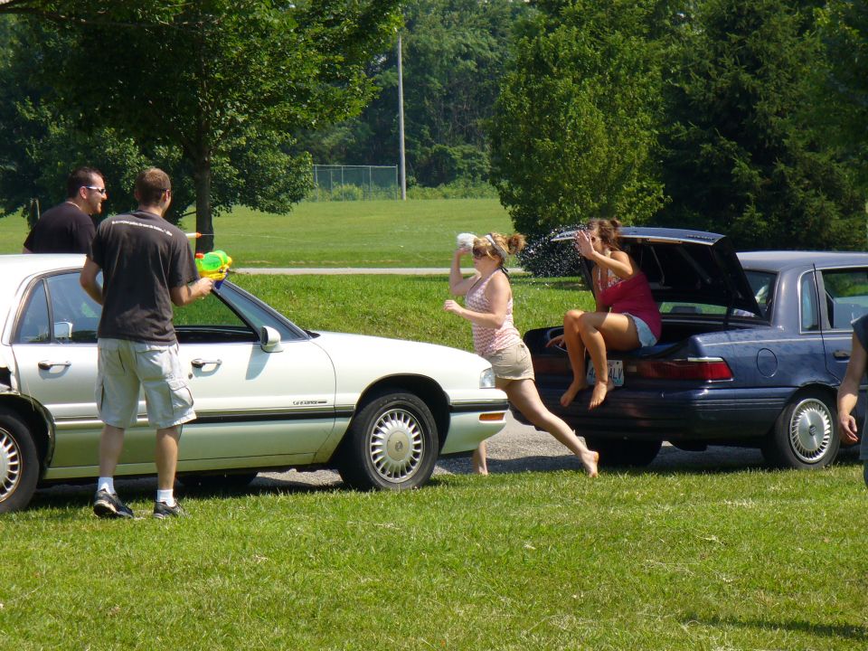 Two cars parked on grass, people with water guns