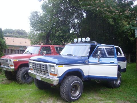 1978 Ford Bronco - Two 1978 Ford Broncos are parked side-by-side on a grassy area with trees and houses in the background.