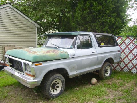 1978 Ford Bronco - This 1978 Ford Bronco has a rusty green hood and is parked in a grassy area next to a fence.