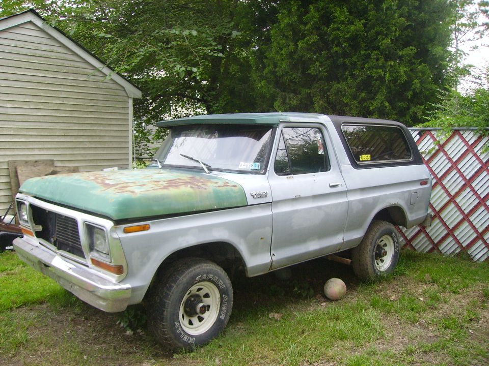 1978 Ford Bronco parked in a yard with a rusty green hood