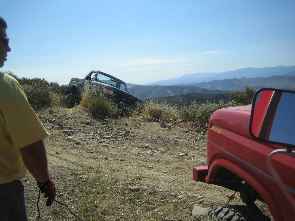 Man watches a lifted truck descend a rocky off-road hill trail