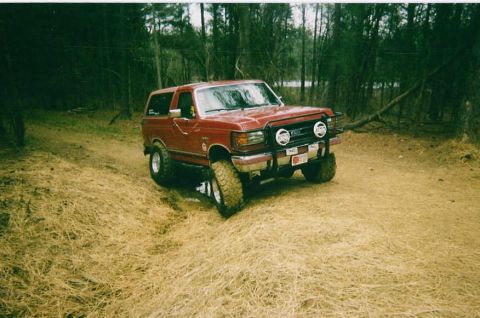 1991 Ford Bronco - This red Ford Bronco is navigating a muddy trail surrounded by trees.