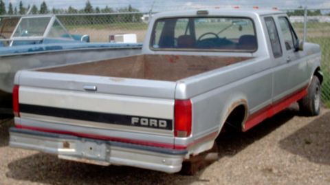 1990 Ford Bronco - Silver Ford pickup truck with red trim, missing rear wheels and tailgate.