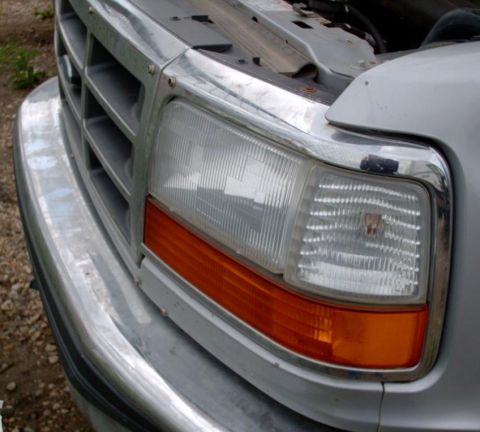 1990 Ford Bronco - Close-up of a silver truck's front end, showing the grille and headlight assembly. The hood is open.