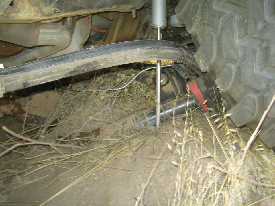 Underside of a lifted truck showing shock, axle and large tire in dirt